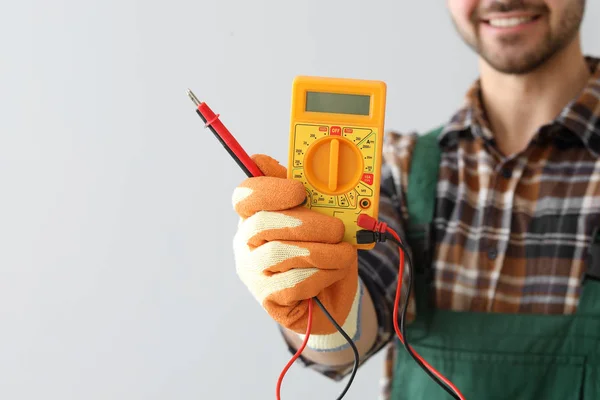 Elettricista maschio con multimetro su sfondo chiaro — Foto Stock