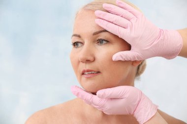 Plastik cerrah hafif arka planda olgun kadının yüzüne dokunmadan