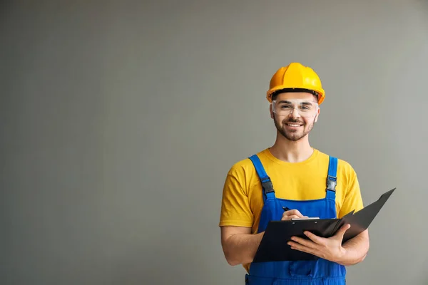 Male electrician with documents on grey background — Stock Photo, Image