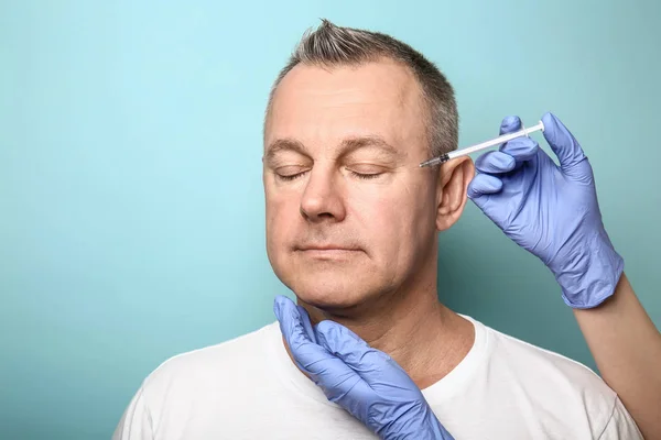 Homem de meia-idade e mãos segurando seringa para injeções anti-envelhecimento em fundo de cor — Fotografia de Stock