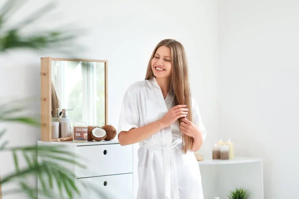 Hermosa mujer joven aplicando aceite de coco en el cabello en casa — Foto de Stock