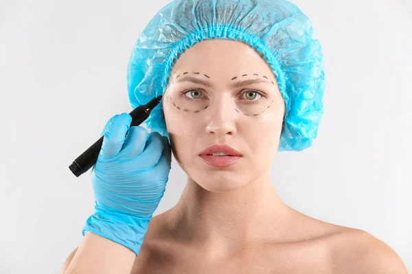 Plastic surgeon applying marking on female face against light background — Stock Photo, Image