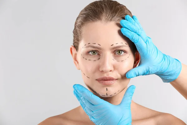 Пластичний хірург торкається обличчя молодої жінки з прикладними слідами на світлому фоні — стокове фото