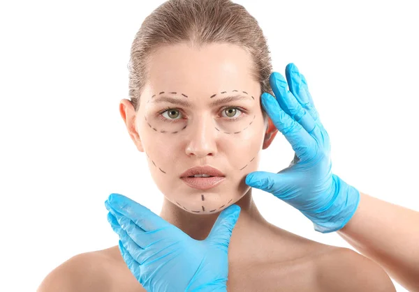 Пластический хирург трогает лицо молодой женщины с нанесенными отметинами на белом фоне — стоковое фото