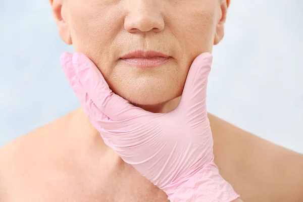 Plastisch chirurg aanraken gezicht van rijpe vrouw op lichte achtergrond, close-up — Stockfoto