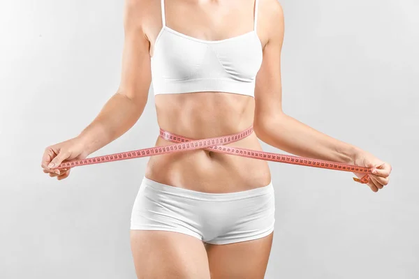 Beautiful young woman with measuring tape on light background. Plastic surgery concept — Stock Photo, Image