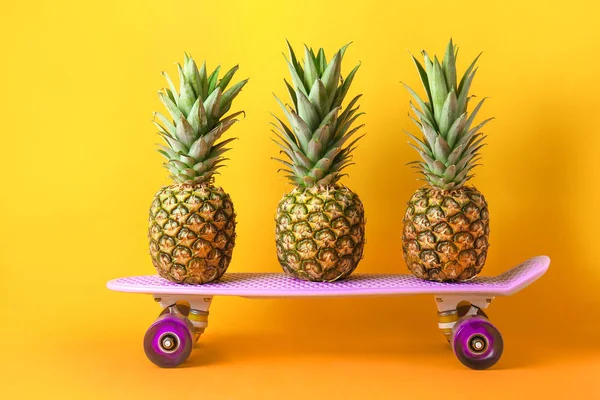 Спелые ананасы и скейтборд на цветном фоне — стоковое фото