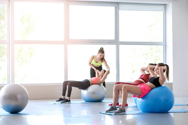 Jovens mulheres esportivas com fitballs fazendo exercícios sob supervisão do treinador no ginásio — Fotografia de Stock