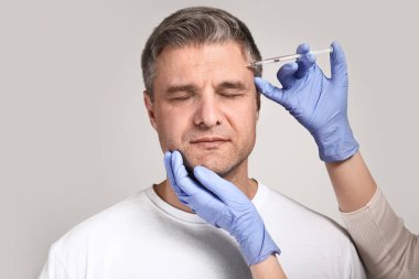 Olgun adam ve elleri gri arka plan üzerinde anti-aging enjeksiyonlar için şırınga tutan