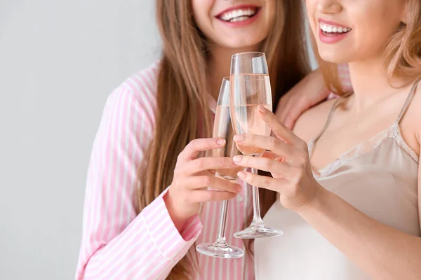 Beautiful young women in pajamas drinking champagne on light background — Stock Photo, Image