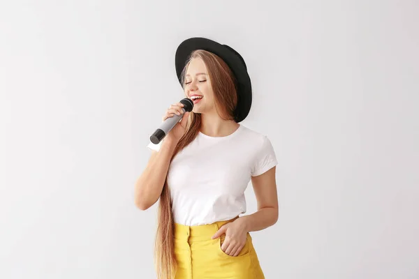 Mooie vrouwelijke zangeres met microfoon op lichte achtergrond — Stockfoto