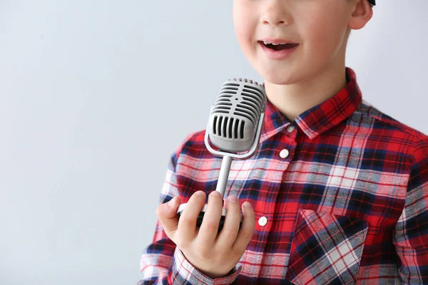 Menino bonito com microfone cantando contra fundo claro — Fotografia de Stock