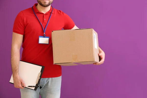Delivery man with box and clipboard on color background — Stock Photo, Image