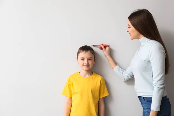 Mother measuring height of her son near wall — Stock Photo, Image