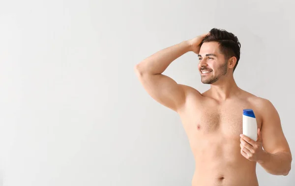 Bonito homem com garrafa de shampoo no fundo claro — Fotografia de Stock