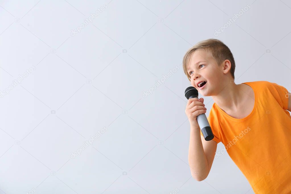 Cute little boy with microphone singing against light background