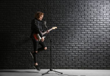 Yakışıklı genç şarkıcı koyu tuğla duvara karşı gitar çalıyor