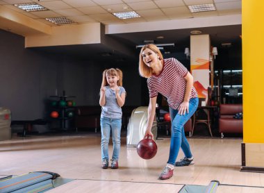 Kadın ve küçük kızı kulüpte bowling oynuyorlar.