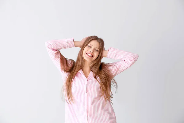 Beautiful young woman in pajamas on light background