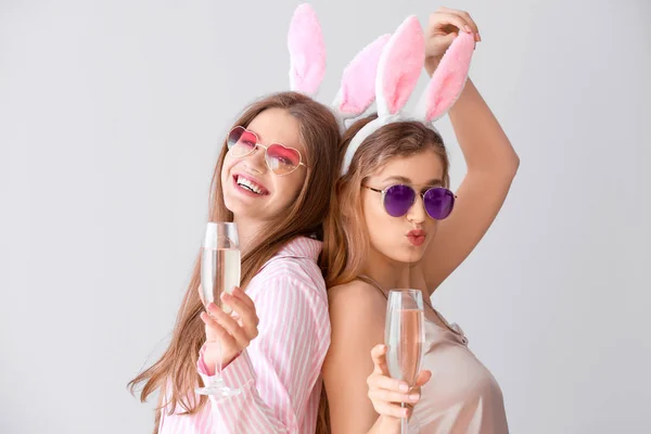 Mooie jonge vrouwen in pyjama en met partij decor drinken champagne op lichte achtergrond — Stockfoto