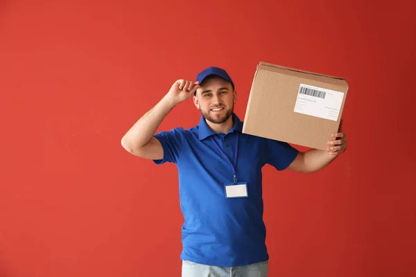 Bonito homem de entrega com caixa no fundo de cor — Fotografia de Stock