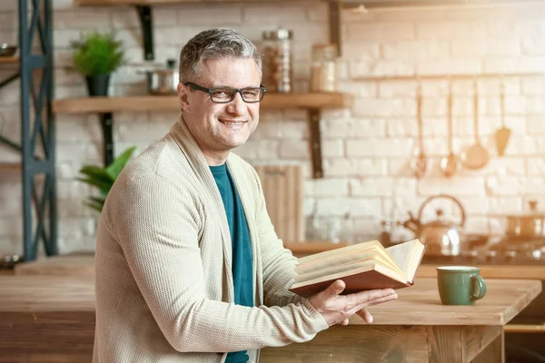 Bello uomo maturo che legge libro in cucina a casa — Foto Stock