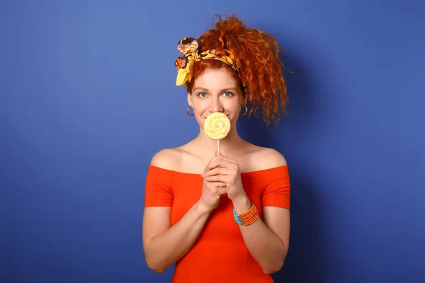 Beautiful redhead woman with lollipop on color background — Stock Photo, Image