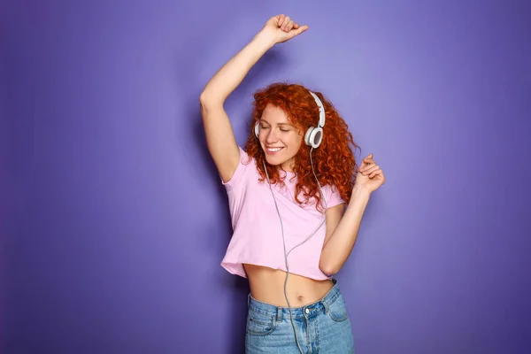 Beautiful redhead woman listening to music on color background — Stock Photo, Image