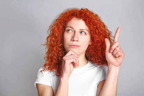 Thoughtful redhead woman with raised index finger on grey background — Stock Photo, Image