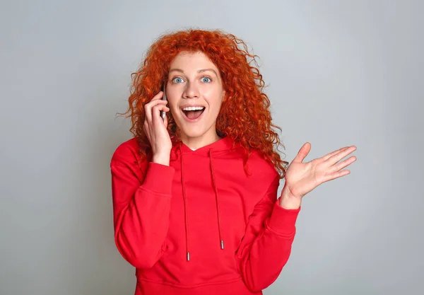 Mooie redhead vrouw praten via de telefoon op grijze achtergrond — Stockfoto