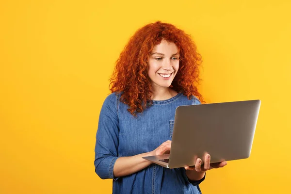 Schöne rothaarige Frau mit Laptop auf farbigem Hintergrund — Stockfoto