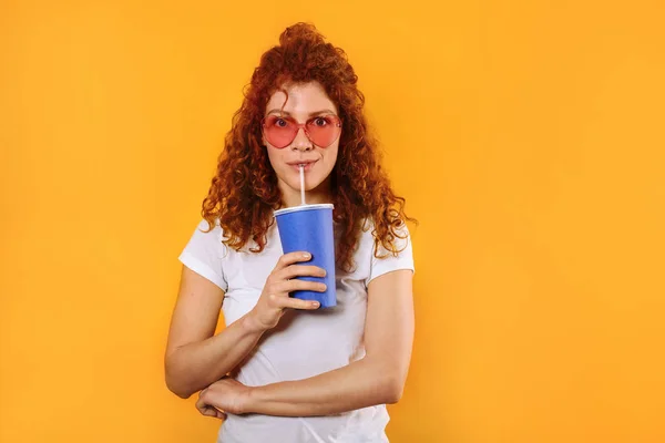 Beautiful redhead woman with drink on color background