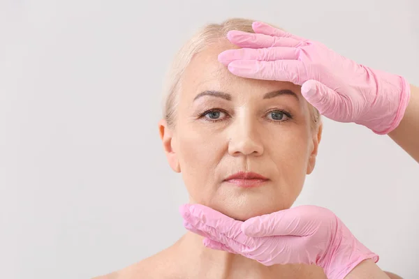 Plastic surgeon touching face of mature woman on light background — Stock Photo, Image