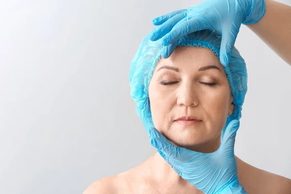 Plastický chirurg dotýkal tvář dospělé ženy na pozadí světla — Stock fotografie
