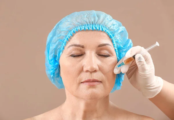 Dospělá žena a ruka plastického chirurga se stříkačkou na barevném pozadí — Stock fotografie