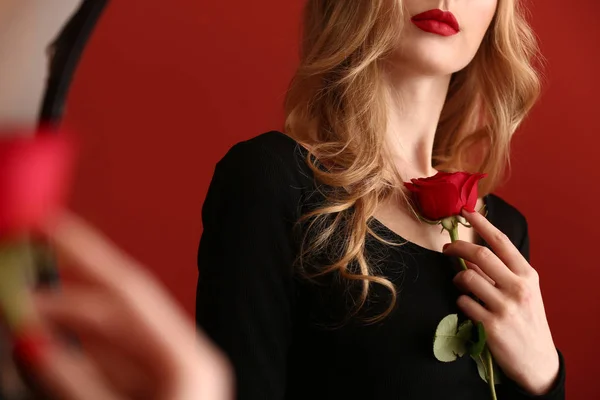 Beautiful young woman with rose flower looking in mirror — Stock Photo, Image