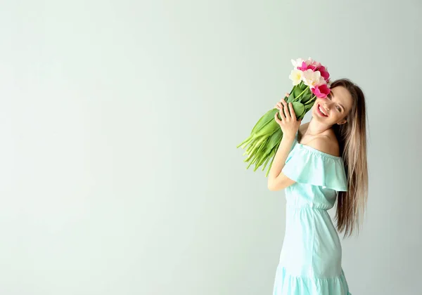 Ung kvinna med bukett av vackra tulpaner på ljus bakgrund — Stockfoto