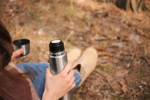 Mulher bebendo chá quente de garrafa térmica na floresta — Fotografia de Stock