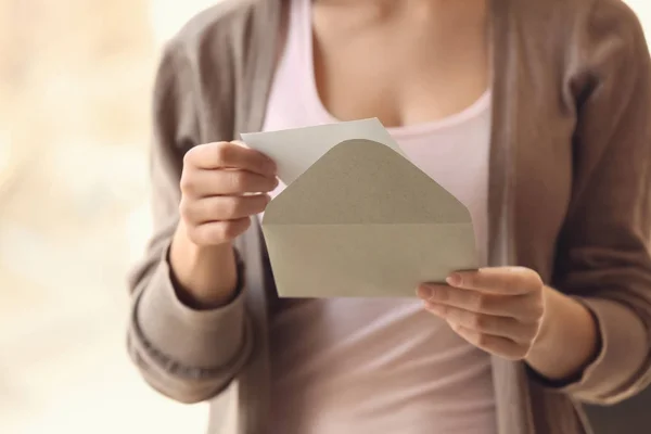 Young woman opening envelope with invitation at home, closeup