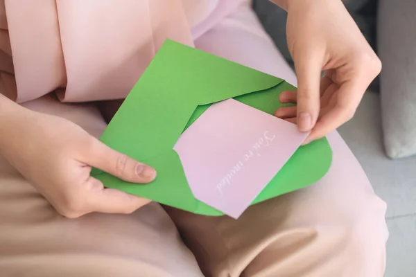 Young woman opening envelope with invitation at home, closeup