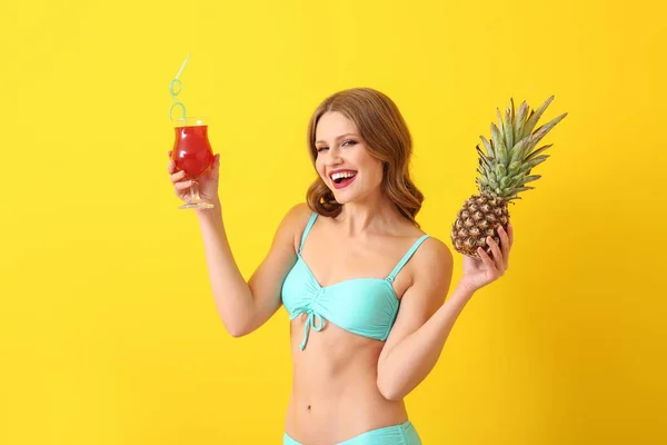 Hermosa mujer joven en traje de baño, con piña y cóctel sobre fondo de color — Foto de Stock