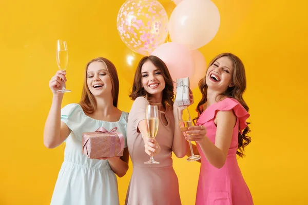 Beautiful young women with glasses of champagne and gifts on color background — Stock Photo, Image