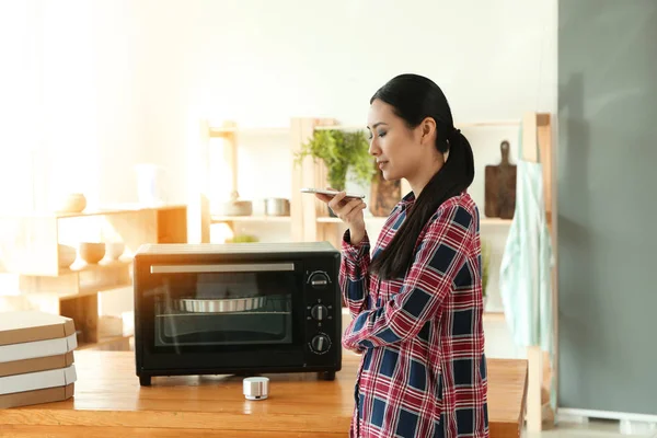 Mujer asiática joven con teléfono móvil en la cocina. Tecnología moderna y domótica inteligente — Foto de Stock