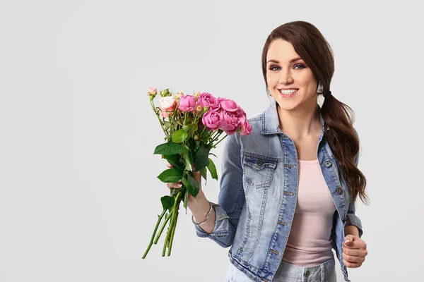 Vacker ung kvinna med bukett blommor på ljus bakgrund — Stockfoto