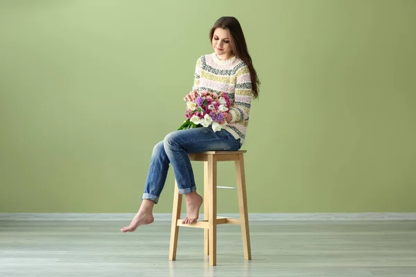 Bella giovane donna con mazzo di fiori seduto sulla sedia contro la parete di colore — Foto Stock