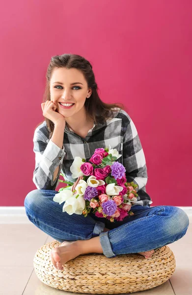 Vacker ung kvinna med bukett blommor sitter på sittpuff mot färg väggen — Stockfoto