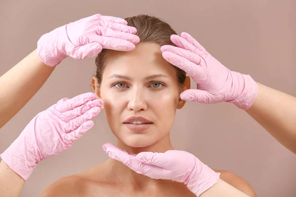Plastic surgeons touching face of young woman on color background — Stock Photo, Image