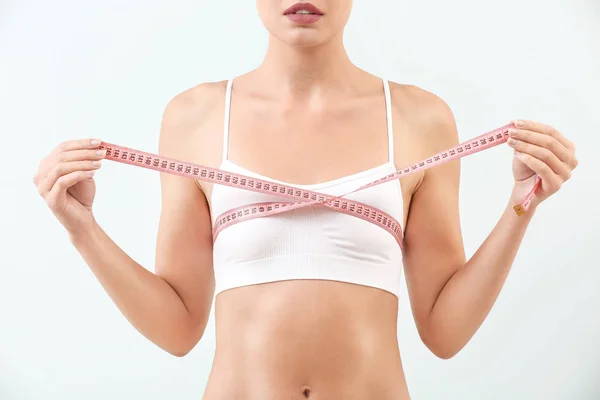 Woman measuring her breast on light background. Concept of plastic surgery — Stock Photo, Image