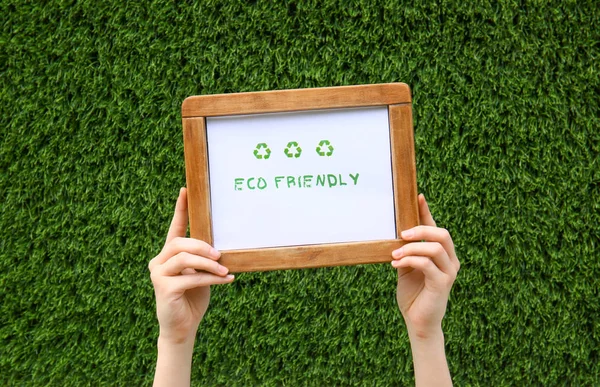 Female hands holding board with text ECO FRIENDLY outdoors
