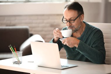 Evde kahve içen dizüstü bilgisayar ile Yakışıklı olgun adam